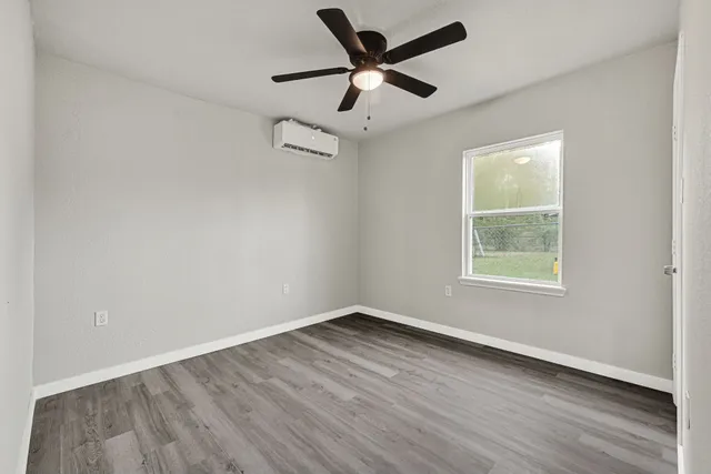 an empty room with wooden floor ceiling fan and windows