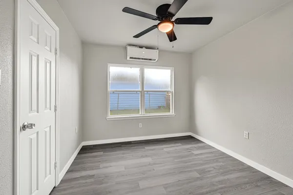 an empty room with wooden floor ceiling fan and windows
