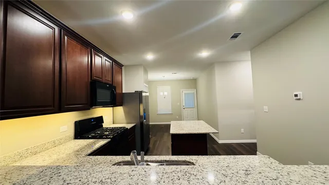 a living room with stainless steel appliances kitchen island granite countertop cabinets a sink and a wooden floor