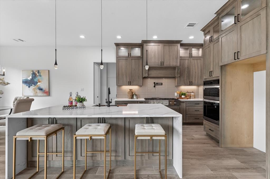 182 Briar Patch Azle, TX 76020 - Photo 10 of 36 Dual tone kitchen featuring light stone counters, a kitchen breakfast bar, pendant lighting, a large island with sink, and stainless steel appliances