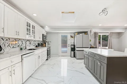 a large white kitchen with kitchen island a large counter top and stainless steel appliances