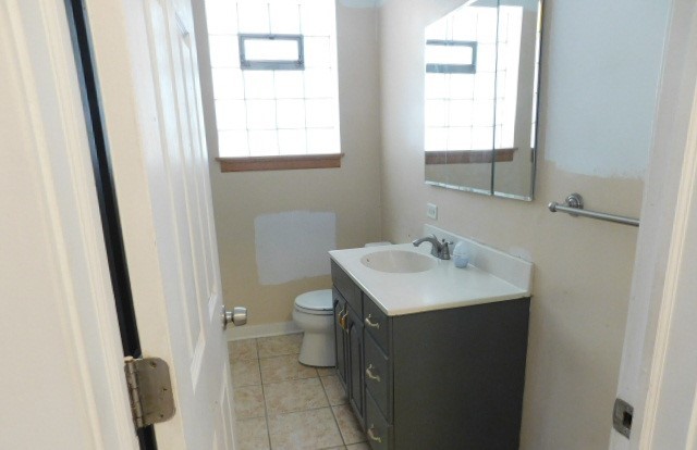 Undisclosed Address Chicago, IL 60630 - Photo 4 of 16 a bathroom with a sink a toilet a mirror and a window