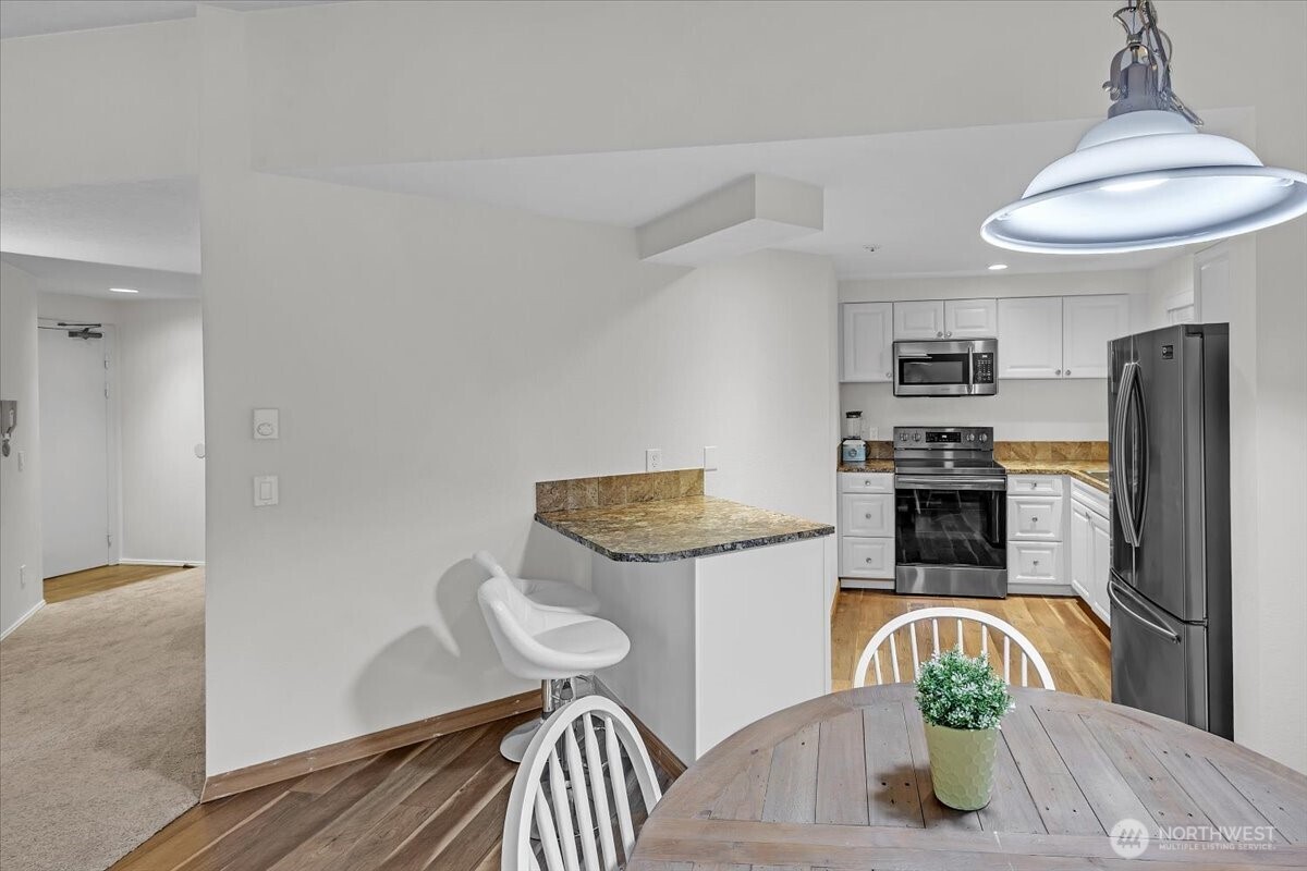 8653 Avondale Road Northeast, Unit D208 Redmond, WA 98052 - Photo 11 of 32 a kitchen with stainless steel appliances kitchen island granite countertop a refrigerator a stove a microwave oven a dining table and chairs with wooden floor