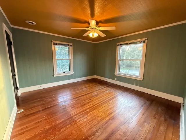 an empty room with wooden floor fan and windows