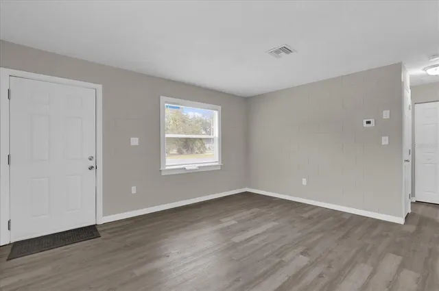 a view of an empty room with wooden floor and a window