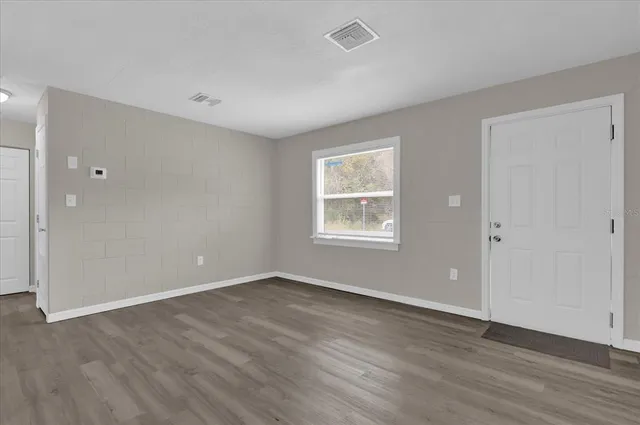 a view of an empty room with wooden floor and a window