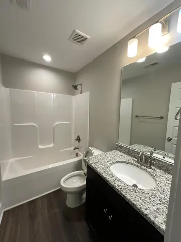 a bathroom with a granite countertop sink a toilet a mirror a bathtub and shower