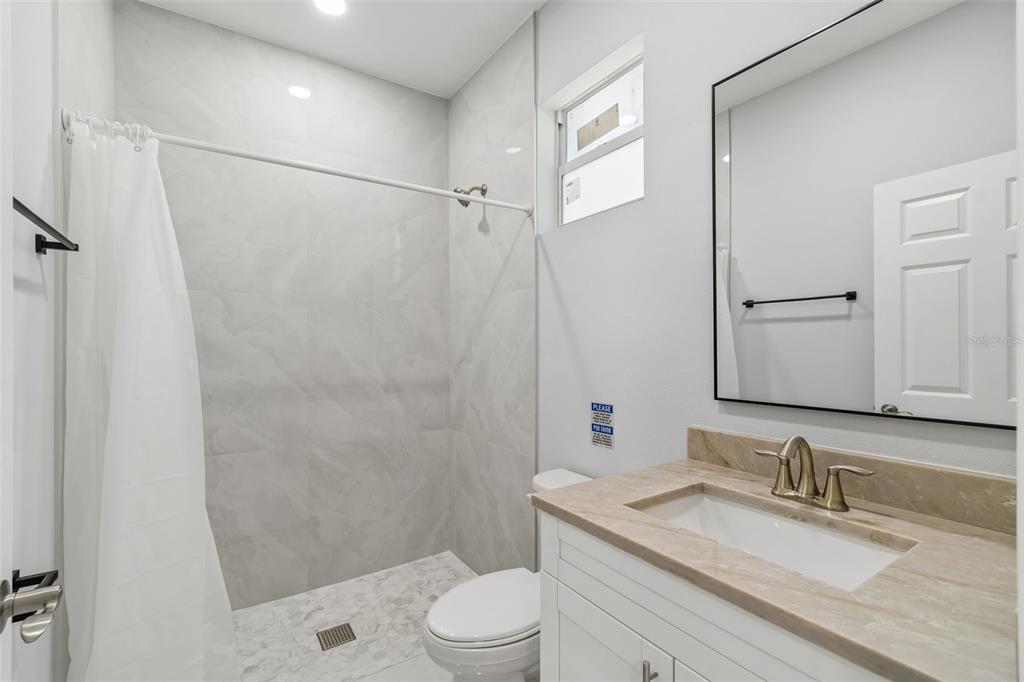 6018 Newmark Street Spring Hill, FL 34606 - Photo 25 of 26 a bathroom with a granite countertop sink toilet a mirror a shower and vanity