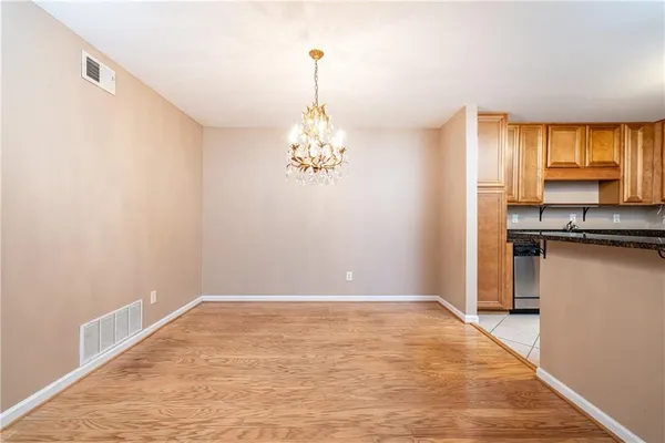 an empty room with chandelier fan and kitchen view