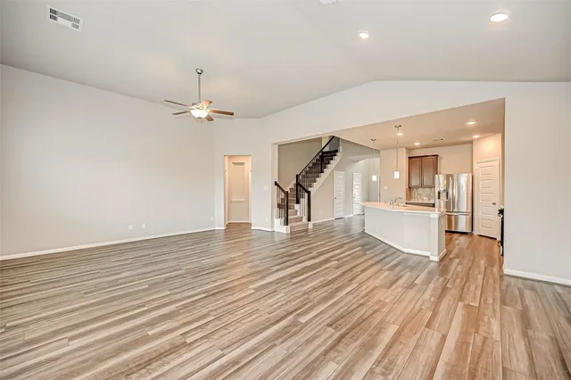 a view of a livingroom with wooden floor a ceiling fan and kitchen space