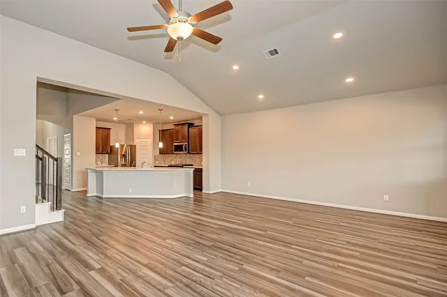 a view of an empty room with wooden floor and a ceiling fan