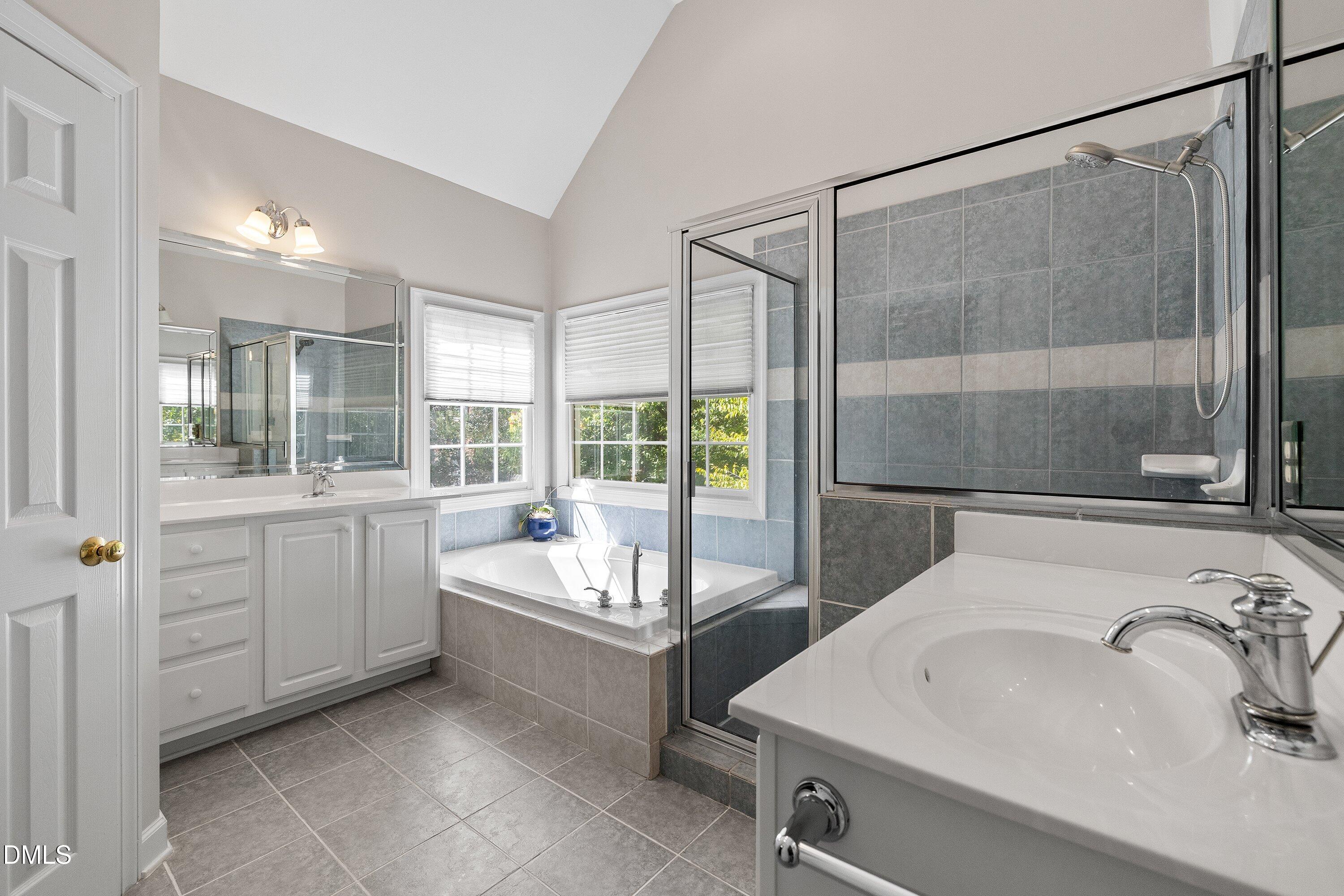 3914 Sterling Ridge Lane Durham, NC 27707 - Photo 35 of 66 Dual vanity with white cabinetry, built-in soaking tub, glass-enclosed shower, tile flooring, and vaulted ceiling