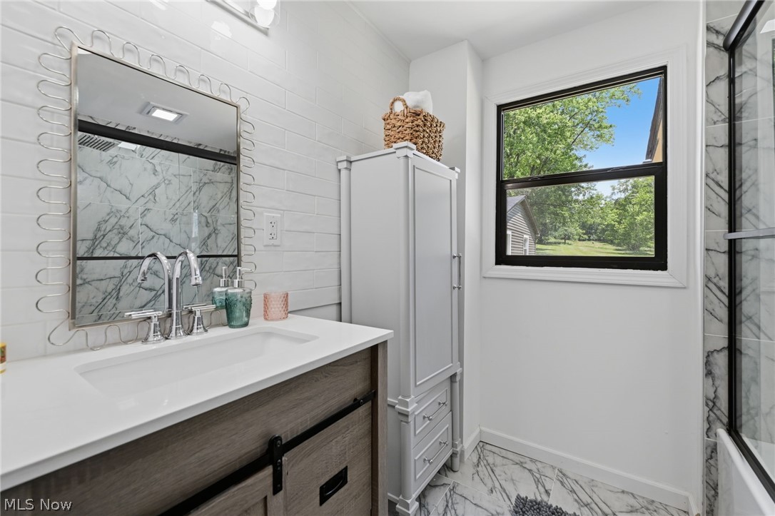 951 Bey Road Akron, OH 44312 - Photo 15 of 34 First floor contemporary bathroom featuring a wood-finish vanity with a white countertop and integrated sink, a rectangular mirror with a decorative frame, a white subway tile backsplash, and marble-patterned floor tiles
