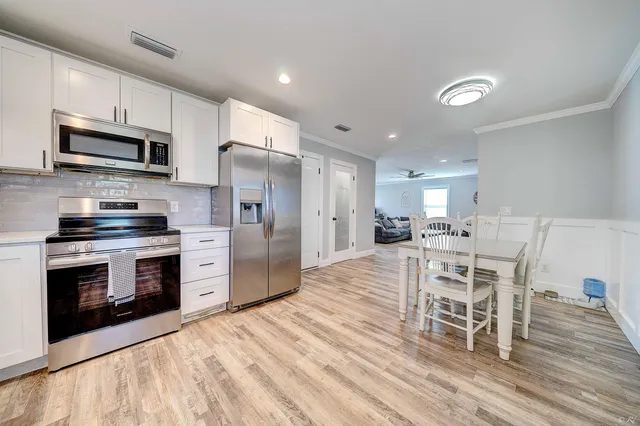 a kitchen with stainless steel appliances a stove a sink dishwasher a refrigerator and a dining table with wooden floor