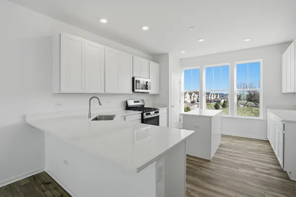 a kitchen with stainless steel appliances granite countertop a sink dishwasher a refrigerator and white cabinets with wooden floor