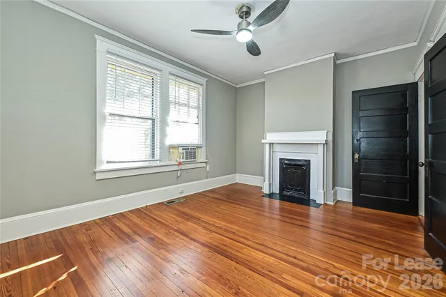 a view of an empty room with wooden floor fireplace and a window