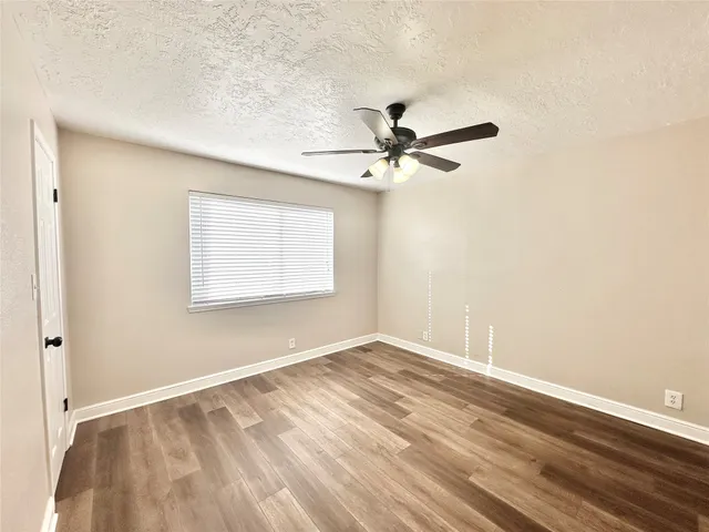 an empty room with wooden floor fan and windows