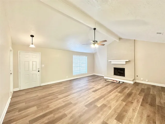 an empty room with wooden floor fireplace and windows