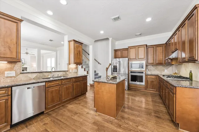 a kitchen with stainless steel appliances granite countertop a stove top oven a sink dishwasher and a refrigerator with wooden floor