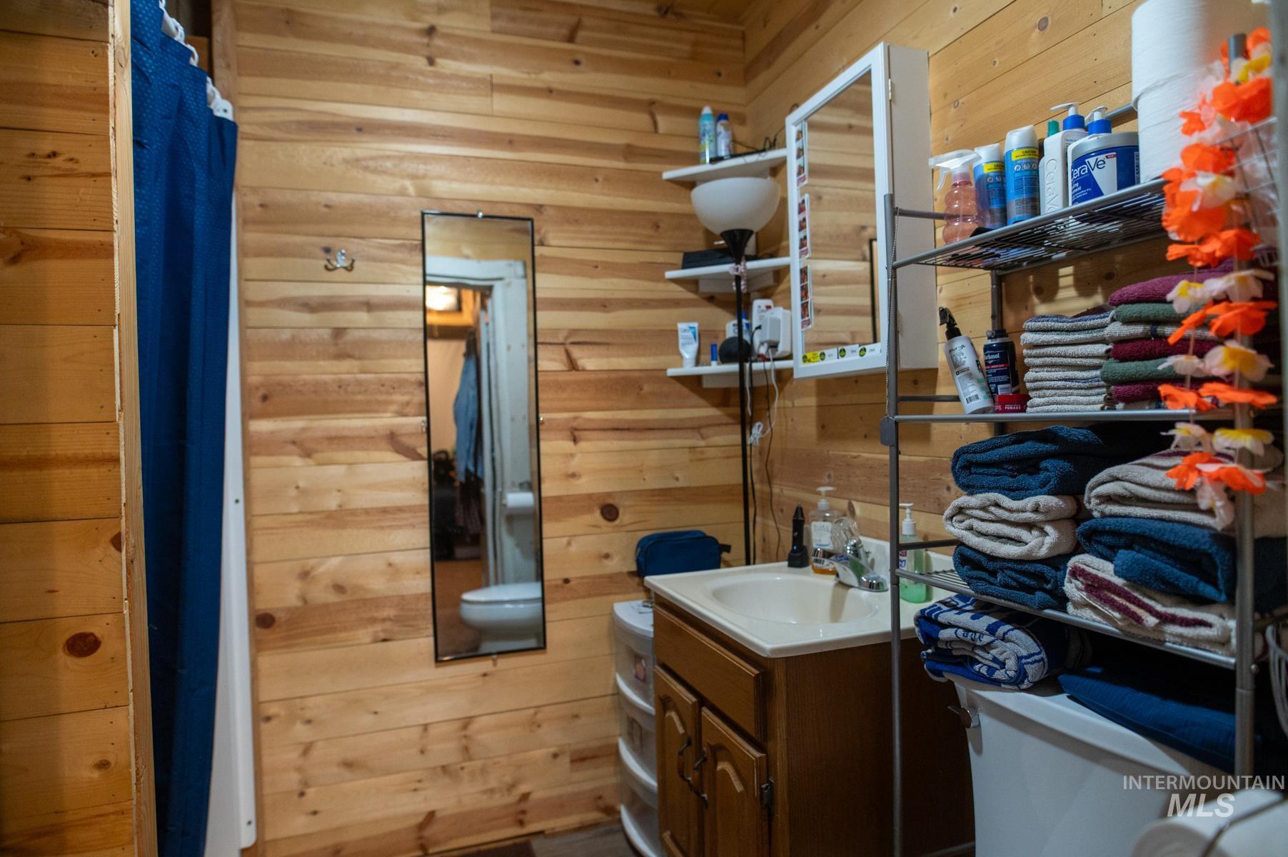 736 East Main Street Weiser, ID 83672 - Photo 29 of 33 Bathroom featuring wood-paneled walls, a single vanity with a cream-colored sink and wood cabinetry, and a wall-mounted mirror