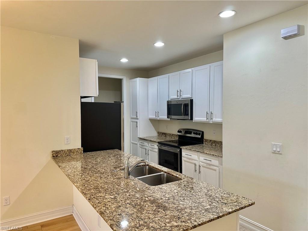 7776 Bristol Circle Naples, FL 34120 - Photo 2 of 6 Kitchen with stainless steel appliances, white cabinetry, light stone countertops, a peninsula, and light wood-type flooring