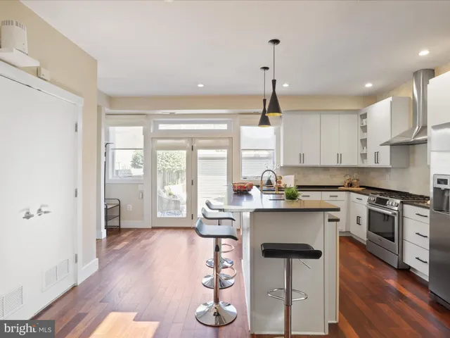 a kitchen with stainless steel appliances granite countertop a stove a refrigerator a sink a dining table and chairs with wooden floor