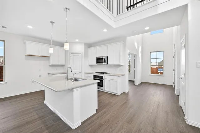 a kitchen with stainless steel appliances granite countertop a sink a stove a refrigerator and island with wooden floor