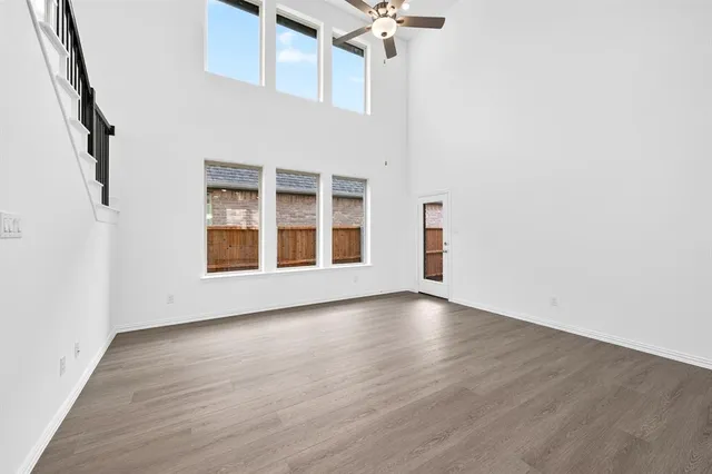 an empty room with wooden floor fan and windows