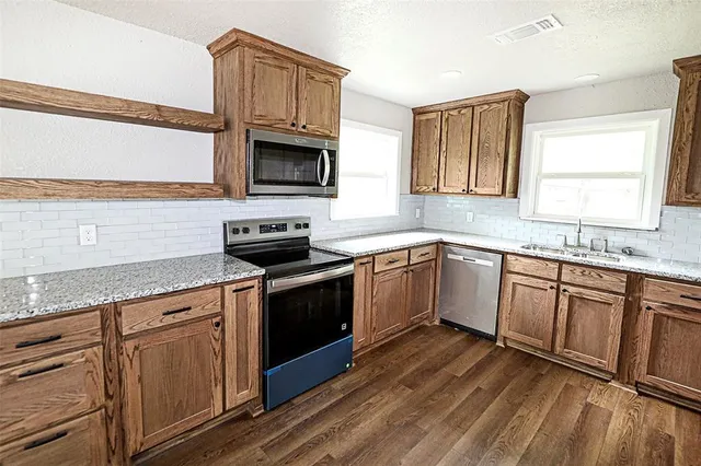 a kitchen with granite countertop a sink dishwasher stove and white cabinets with wooden floor