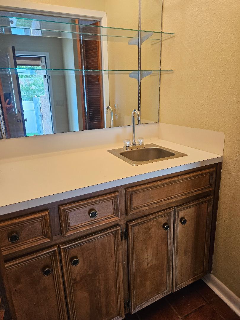 16 North Ave A, Unit B Elgin, TX 78621 - Photo 6 of 17 Wet bar just between the living room and the dining room, featuring a stainless steel sink, a chrome faucet, a white countertop, and wood cabinetry with dark hardware