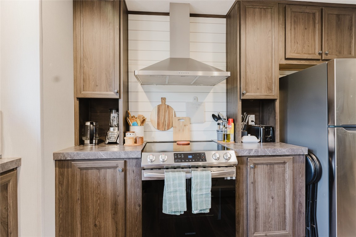 400 St Johns Road Dale, TX 78616 - Photo 4 of 17 Kitchen featuring stainless steel appliances, wall chimney exhaust hood, light countertops, tasteful backsplash, and brown cabinetry
