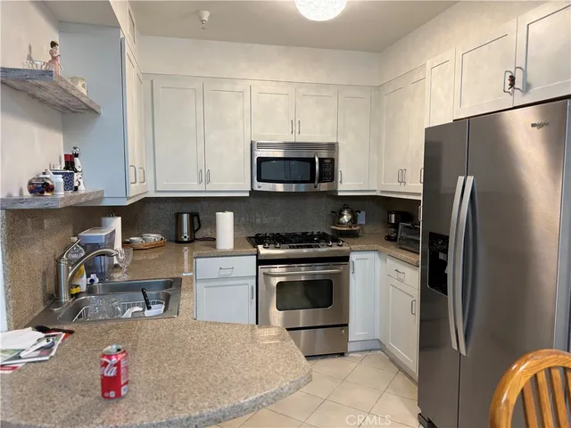 a kitchen with stainless steel appliances granite countertop a refrigerator stove a sink dishwasher and white cabinets with wooden floor