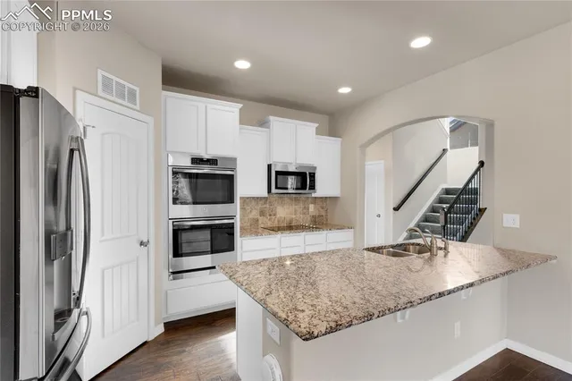 a kitchen with stainless steel appliances granite countertop a sink a microwave a refrigerator and white cabinets