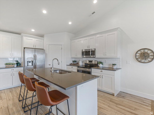 1278 South Grace Way Layton, UT 84041 - Photo 8 of 23 Modern kitchen featuring an island with an undermount sink, stainless steel appliances, white shaker-style cabinetry, subway tile backsplash, and wood-finish flooring