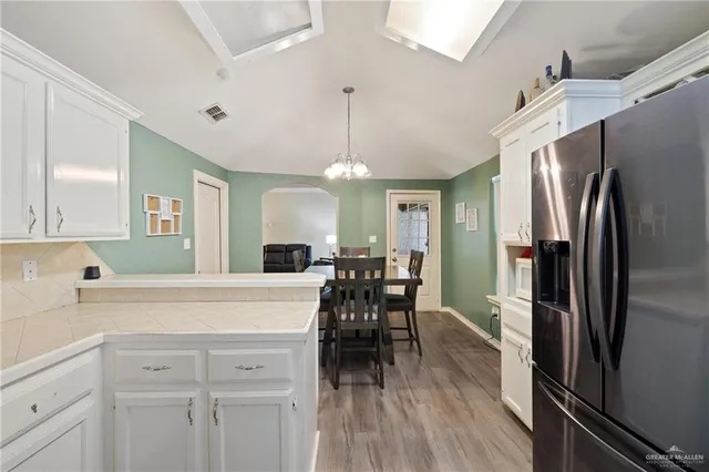 a kitchen with stainless steel appliances a refrigerator a sink dishwasher a stove and white cabinets with wooden floor