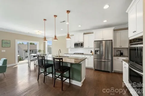 a kitchen with stainless steel appliances a dining table chairs stove refrigerator and cabinets