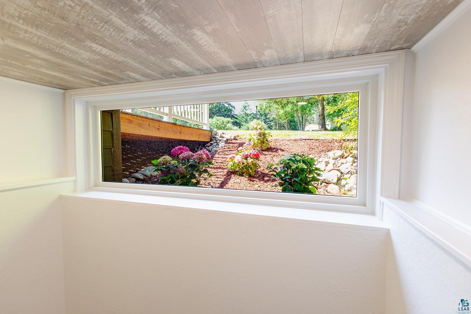 29 Ridge Road Esko, MN 55733 - Photo 25 of 41 White-trimmed window looking out to a landscaped garden with flowering shrubs, mulched beds, and stone accents