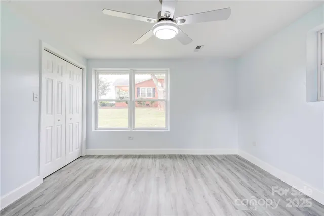 an empty room with wooden floor ceiling fan and windows