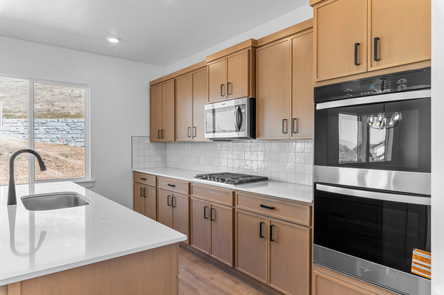 1341 West 2350 South, Unit 10 Perry, UT 84302 - Photo 7 of 18 Modern kitchen featuring wood-finish cabinetry with black hardware, white subway tile backsplash, stainless steel appliances, and a gas cooktop