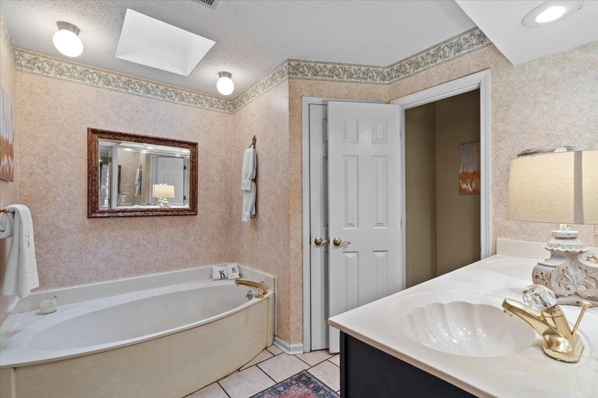 732 North Tree Drive Collierville, TN 38017 - Photo 25 of 40 Bathroom featuring light tile patterned floors, a skylight, double vanity, a garden tub, and wallpapered walls