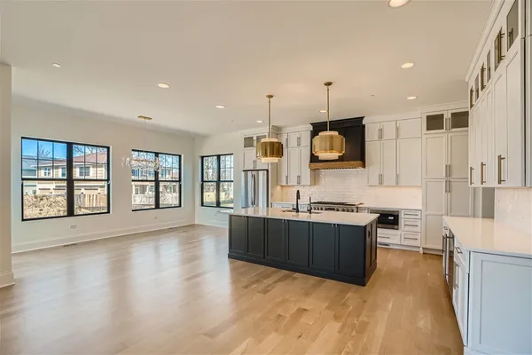 a large kitchen with kitchen island a stove a sink a refrigerator and white cabinets with wooden floor