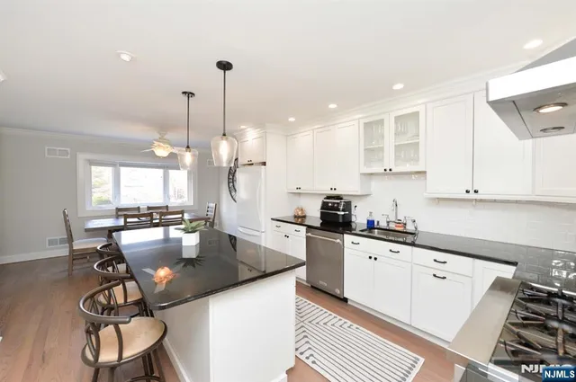 a kitchen with stainless steel appliances granite countertop a sink stove and white cabinets with wooden floor