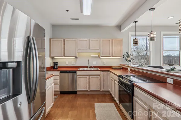 a kitchen with stainless steel appliances granite countertop a refrigerator a sink dishwasher a stove and white countertops with wooden floor