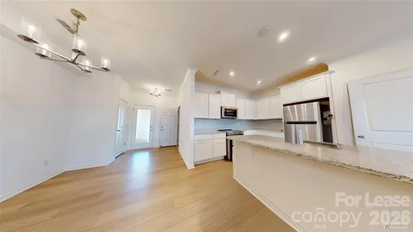 a large white kitchen with a refrigerator a stove a sink dishwasher a dining table and chairs with wooden floor