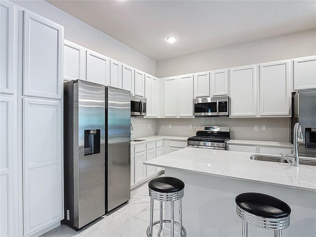 1326 Butterfly Orchid Road Davenport, FL 33837 - Photo 14 of 54 a kitchen with stainless steel appliances granite countertop a refrigerator a stove a sink and white cabinets with wooden floor