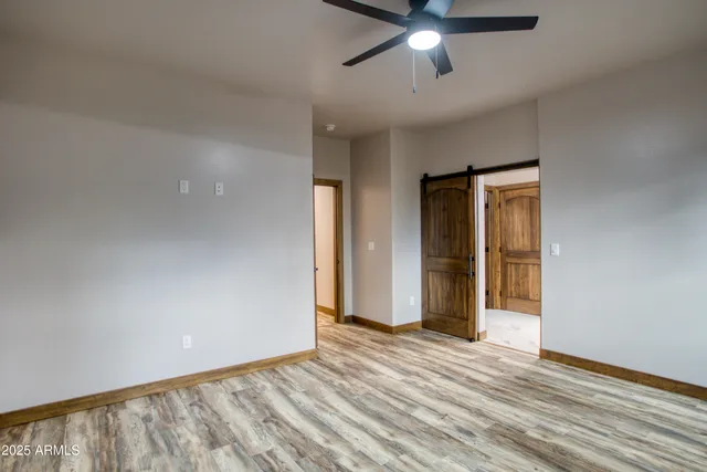 a view of an empty room with wooden floor and a ceiling fan
