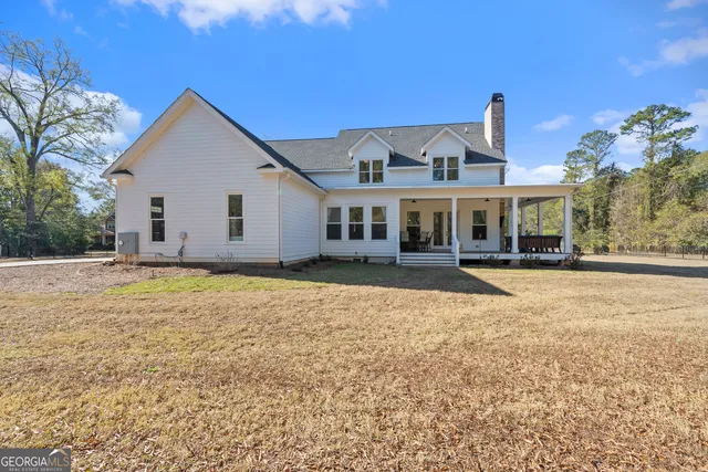 a view of a white house with a large pool and lawn chairs under an umbrella