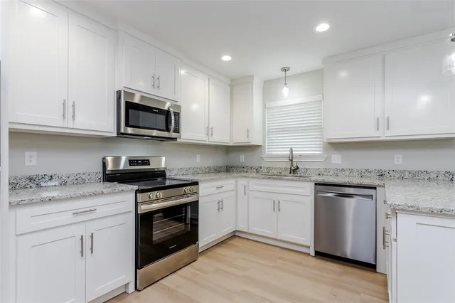 a kitchen with granite countertop white cabinets sink and stainless steel appliances