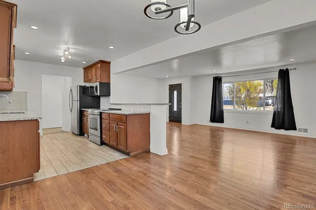 a kitchen with stainless steel appliances granite countertop a sink a stove top oven and a wooden floor