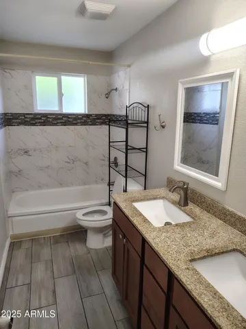 a bathroom with a granite countertop sink toilet and painting on the wall